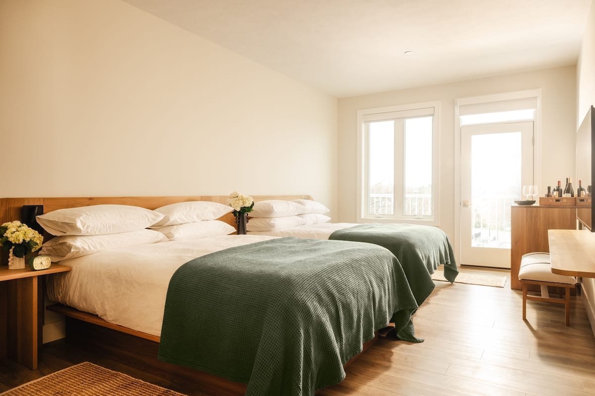 A bedroom with two beds, a wooden desk, a chair, and a balcony with a view.