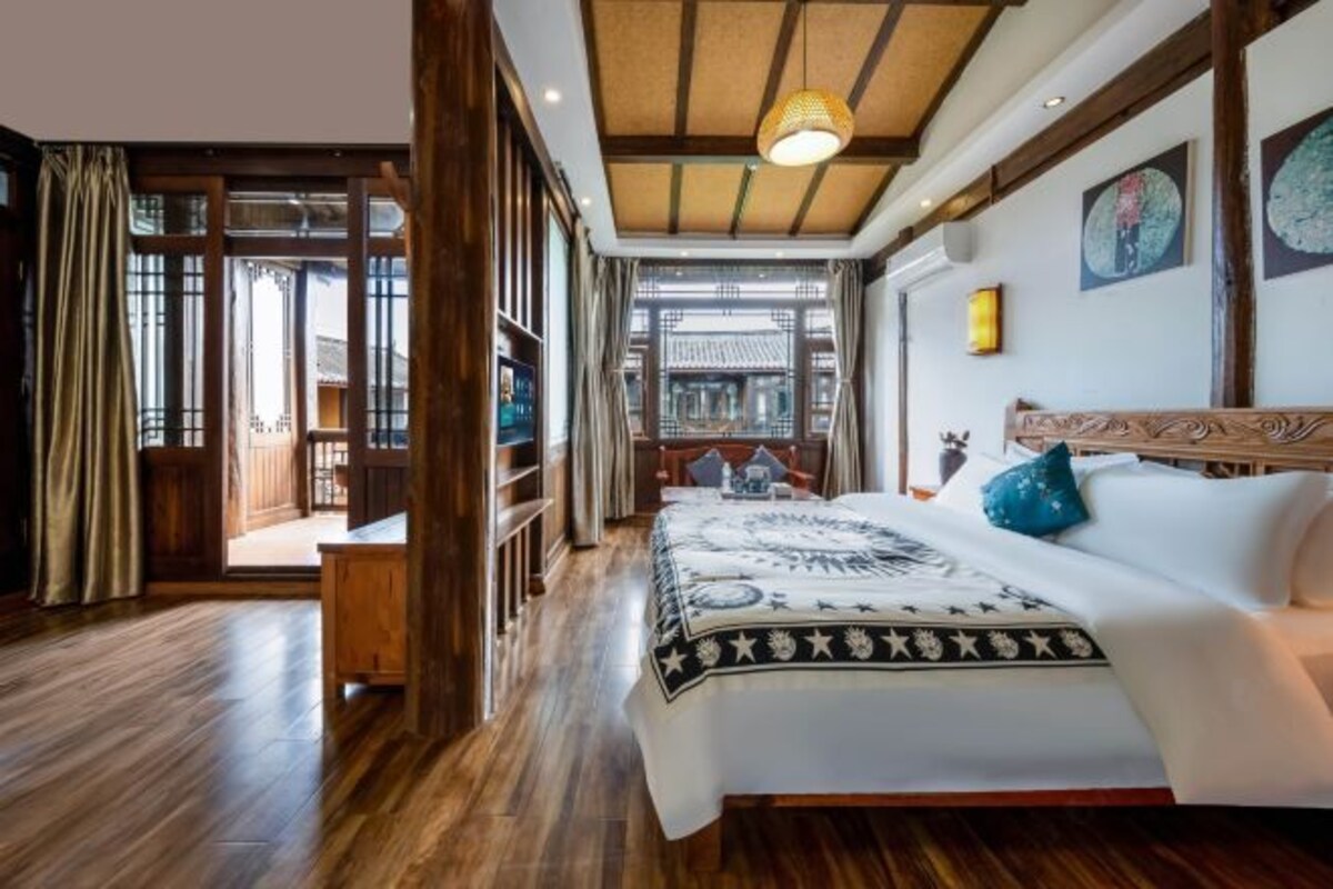 A traditional-style bedroom with a large bed, wooden flooring, and a view through an open door.