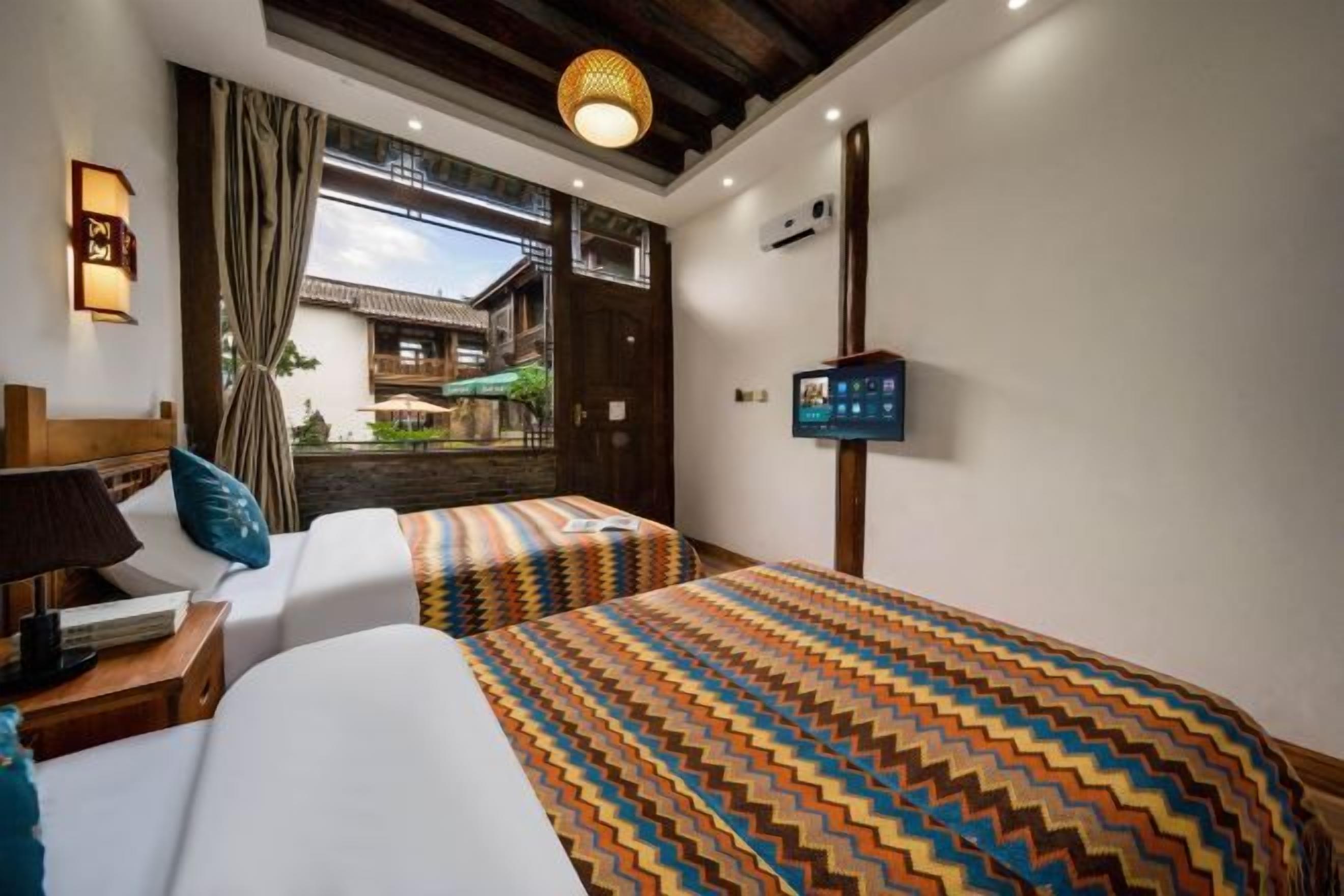 A hotel room with two beds, a TV, a desk with a lamp, and a view of a courtyard.