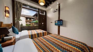 A hotel room with two beds, a TV, a desk with a lamp, and a view of a courtyard.