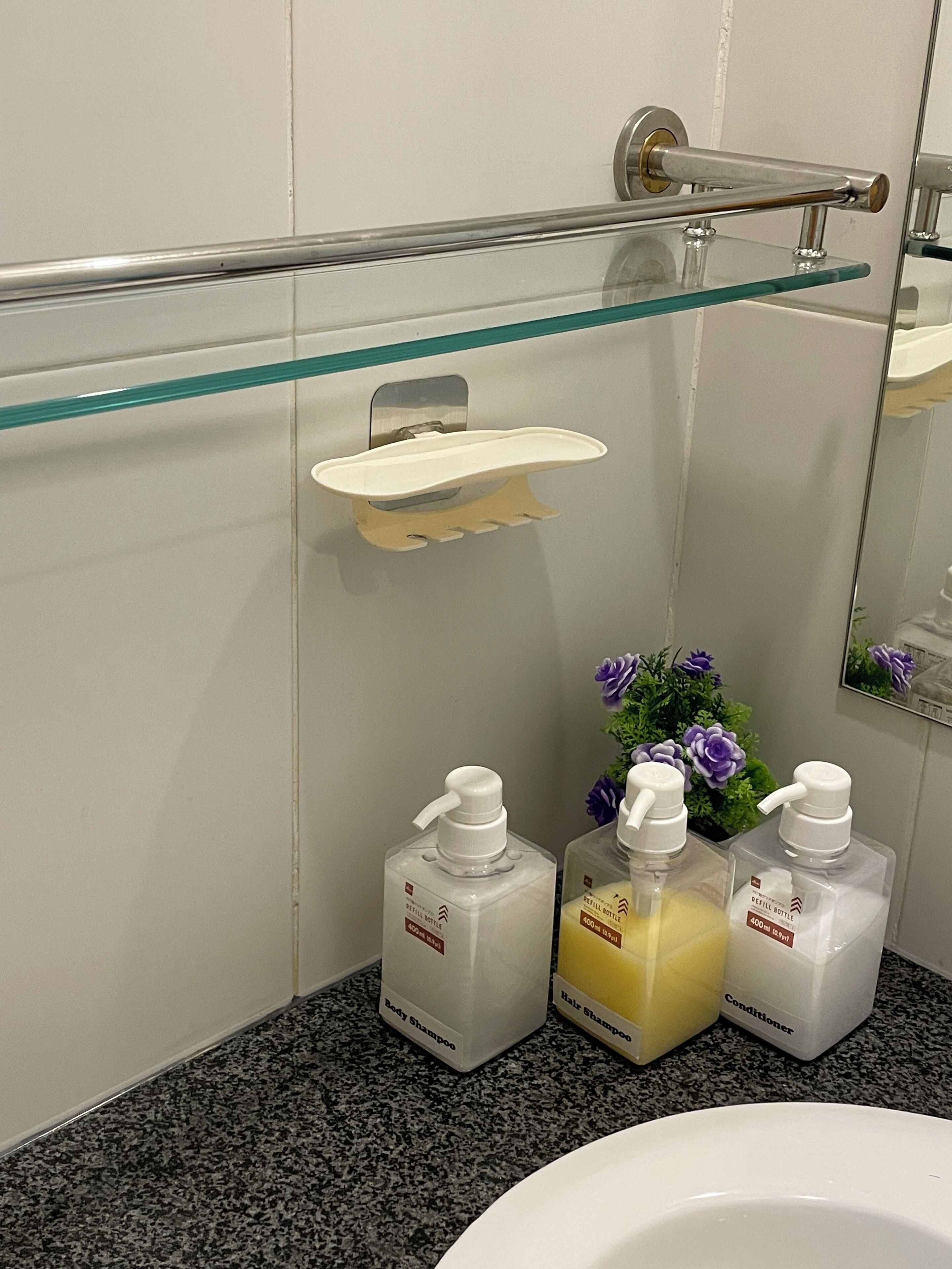 A bathroom with a glass shelf, a sink, and three bottles of toiletries.