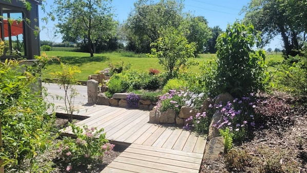 A wooden deck leading to a garden with various plants and flowers.