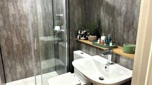 Un baño moderno con ducha envuelta en vidrio, un lavamanos blanco y un estante con artículos de aseo.