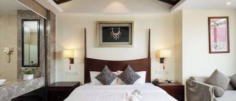 A hotel room with a large bed, two bedside tables, a nightstand, a mirror, a framed picture on the wall, and a sofa.