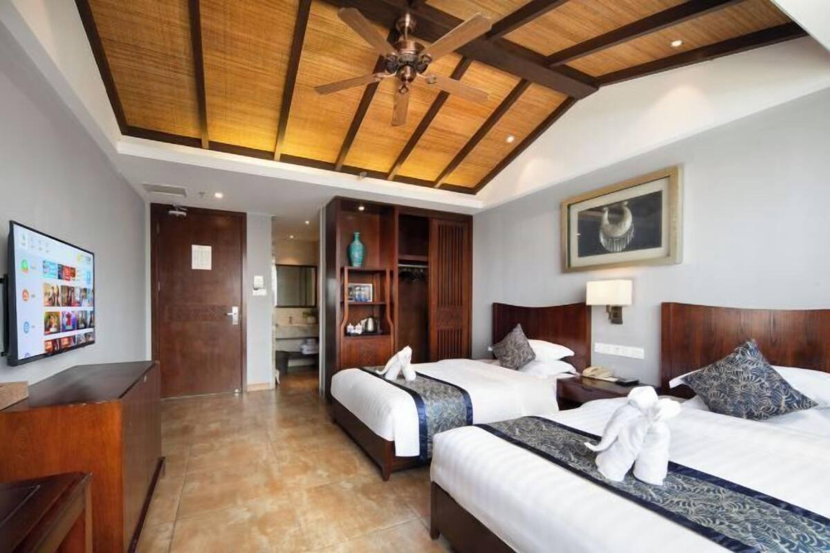 Habitación de hotel con dos camas, ventilador de techo, televisión y techo de madera.