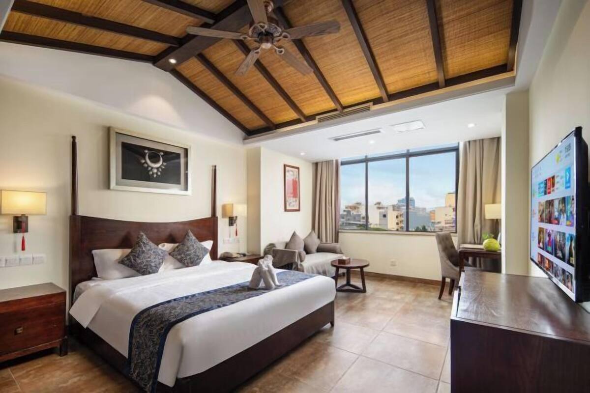 Habitación de hotel con una cama grande, ventilador de techo, escritorio y vista a la ciudad.