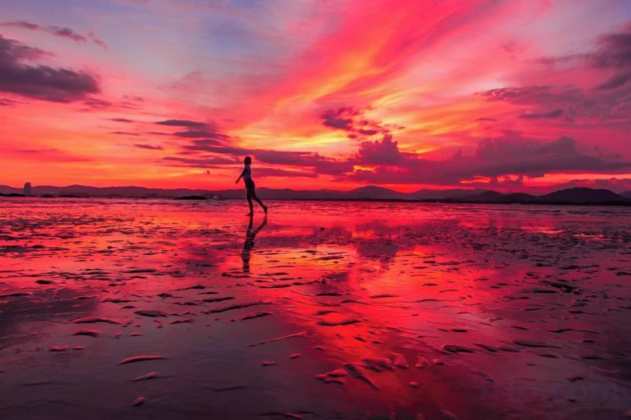 A sunset over a beach with a person walking.