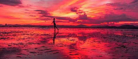 Atardecer sobre una playa con una persona caminando.