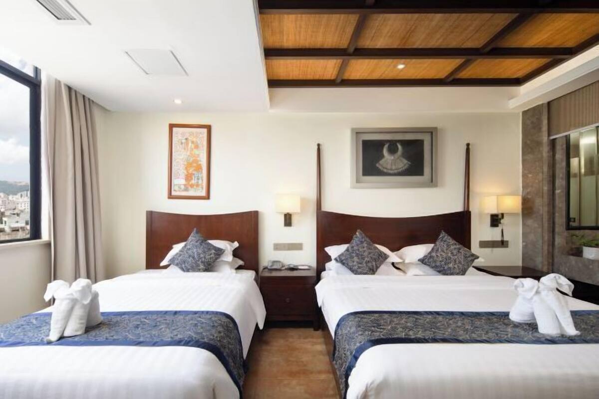 Habitación de hotel con dos camas, vista a la ciudad, techo de madera y obras de arte en las paredes.