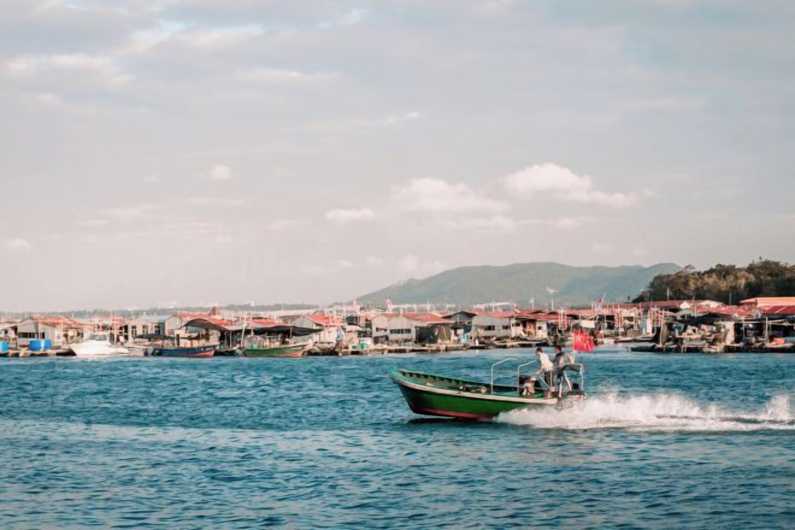 A boat on a body of water with a waterfront area in the background.
