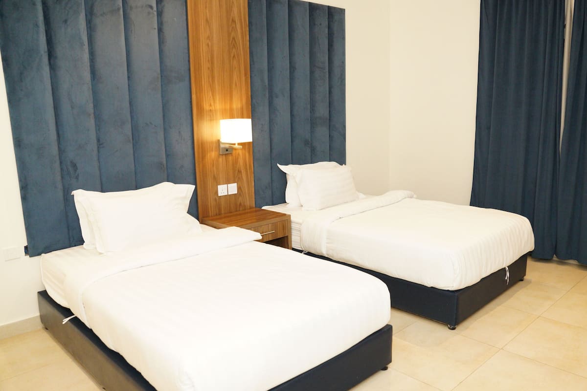 A hotel room with two single beds, a wooden headboard, a nightstand, and a wall-mounted lamp.
