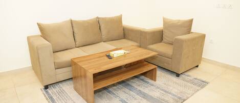 A beige sofa with a wooden coffee table in a room with tiled flooring and a patterned rug.