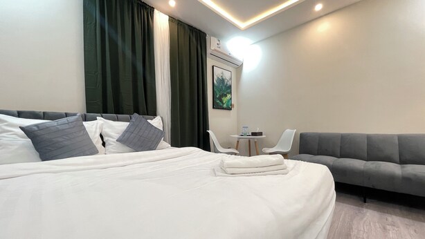 A modern hotel room with a large bed, a grey sofa, and a small table with a chair. - AQ 21 New Studio with kitchen and self check-in (Riyadh)