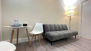 A hotel room with a grey sofa, a white chair, a small table with water bottles and a tissue box, and a floor lamp. - AQ 21 New Studio with kitchen and self check-in (Riyadh)