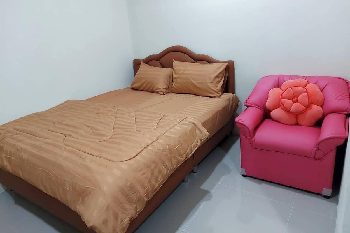 Ein Einzelbett mit Kopfstütze, ein rosa Stuhl mit blumigem Kissen und eine schlichte weiße Wand.