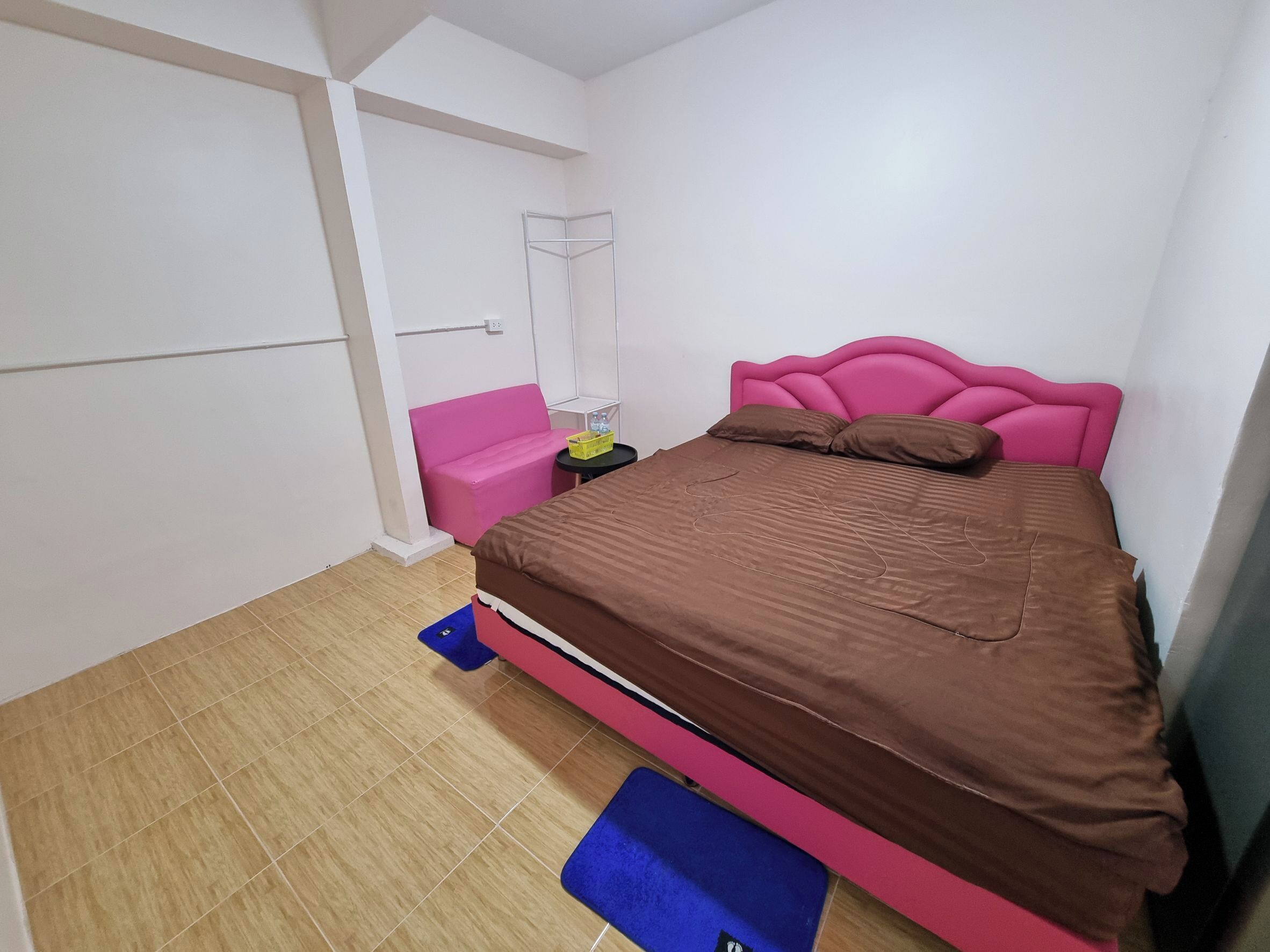 Quarto com cama, mesa de cabeceira, uma cadeira rosa e uma pequena mesa com um cesto.