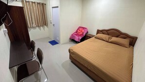 A bedroom with a bed, a desk, a chair, a fan, and a door. - NOPPHADON HOTEL (Bangkok)