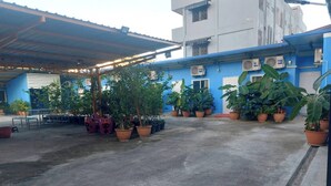 A covered outdoor area with potted plants and a building with blue walls and air conditioning units. - NOPPHADON HOTEL (Bangkok)
