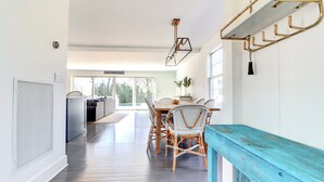 A modern interior with a dining area featuring wicker chairs, a wooden table, and a blue bench. - 5 Bedrooms! 4 Min to the Beach! HEATED POOL! (Westhampton Beach)