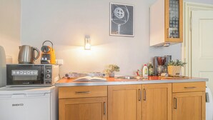 Cocina compacta con microondas, hervidor de agua y cafetera sobre la encimera. Cuenta con un lavamanos, un mueble pequeño y una fotografía enmarcada en la pared.