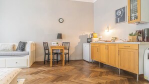 Un espacio habitable compacto con kitchenette, comedor y zona de estar con sofá y mesa.