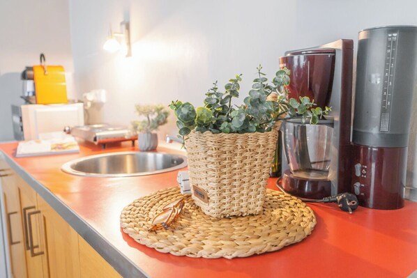 A kitchen counter with a woven basket containing green plants, a coffee maker, and a scale.