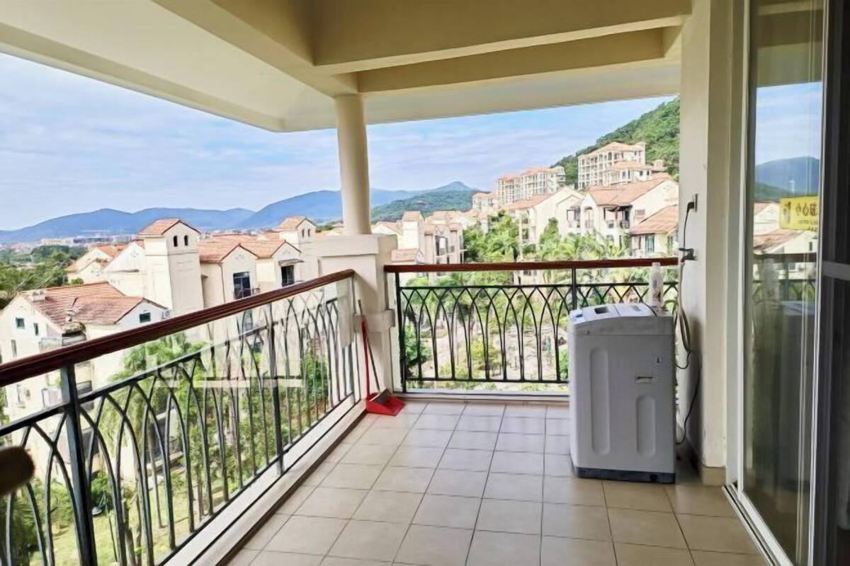 A balcony with a washing machine, a railing, and a view of buildings and mountains.