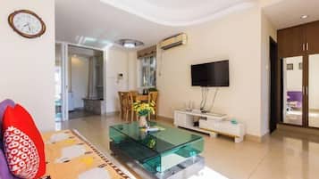 Una sala moderna con una mesa de centro de vidrio, un televisor de pantalla plana y un comedor al fondo.