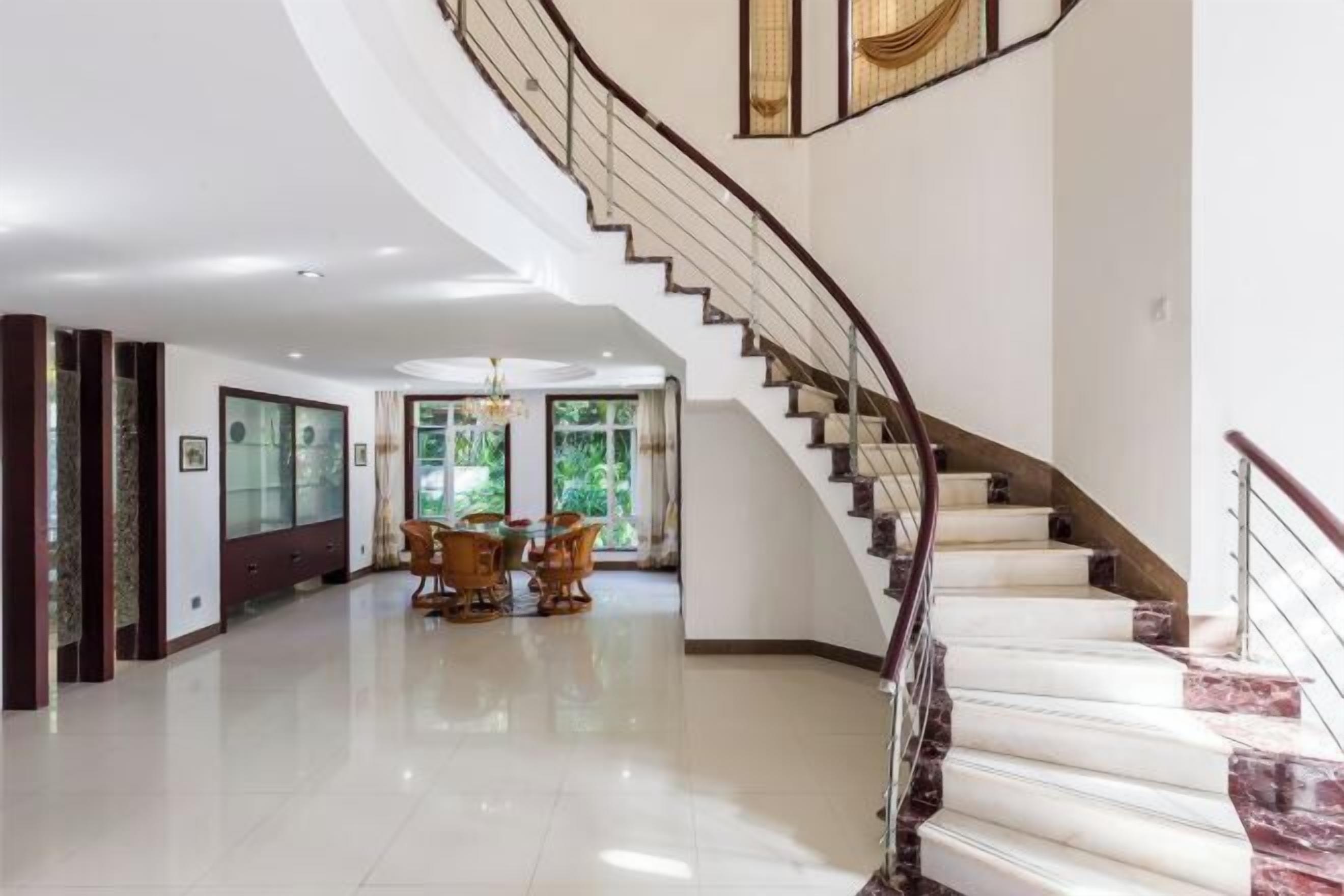 Un intérieur spacieux avec un escalier en colimaçon, un coin repas avec des chaises et une vue sur la verdure environnante.
