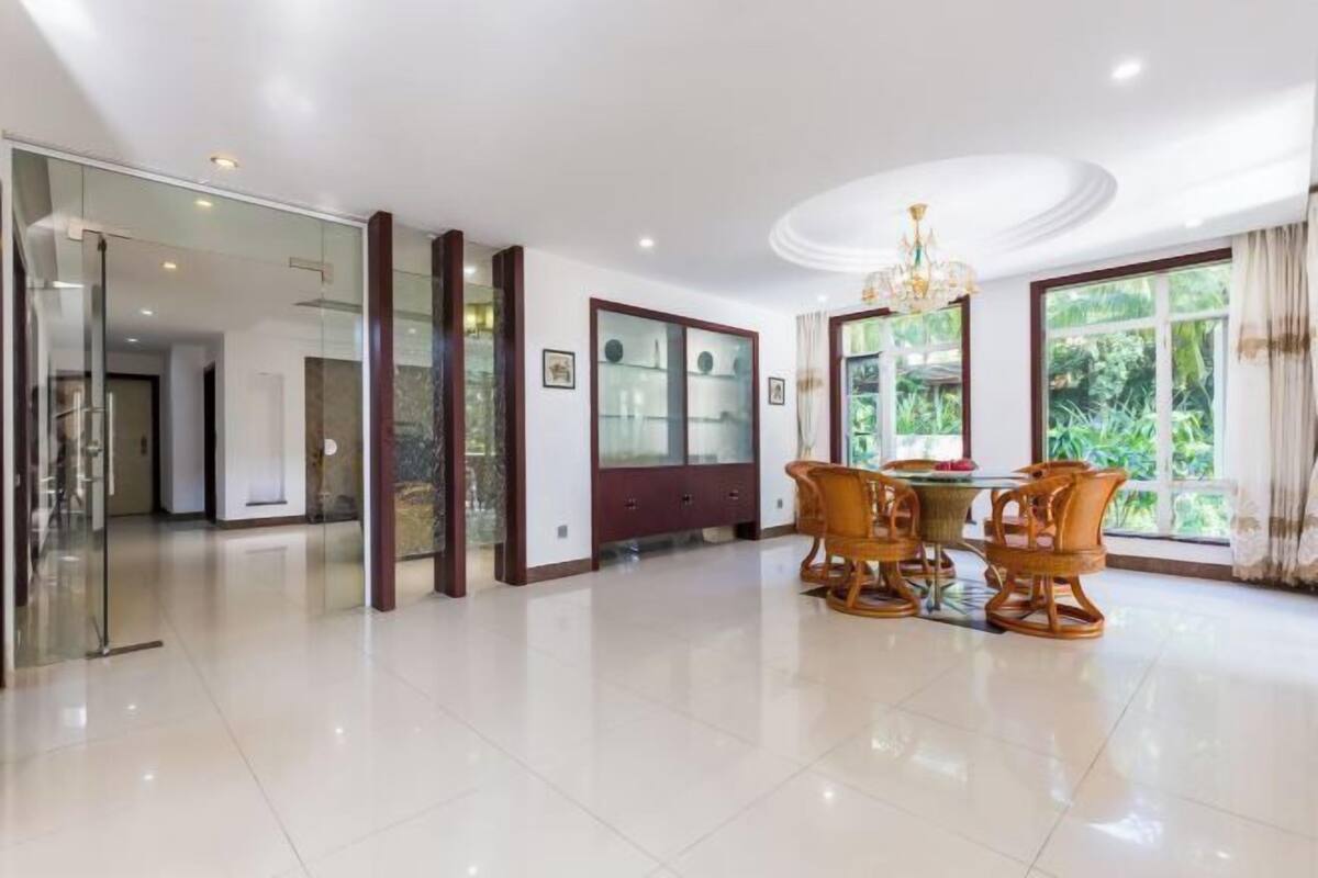 A spacious room with a dining area, a glass partition, and a view of greenery outside.