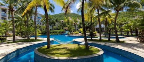 A swimming pool surrounded by palm trees and a building in the background.
