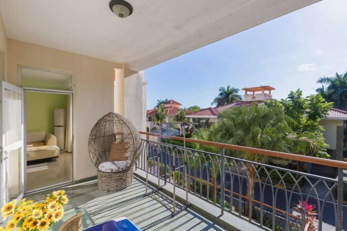 A balcony with a wicker chair, a view of neighboring houses, and a railing.