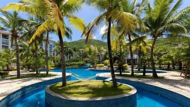 A resort pool surrounded by palm trees and a herringbone pool design. - Renda Holiday Apartment (Sanya)