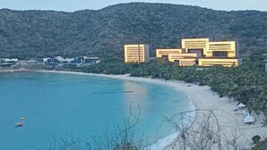 A coastal area with modern buildings, a beach, and a forested hill in the background. - Renda Holiday Apartment (Sanya)