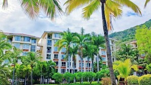 A multi-story hotel with balconies, surrounded by palm trees and a pool. - Renda Holiday Apartment (Sanya)