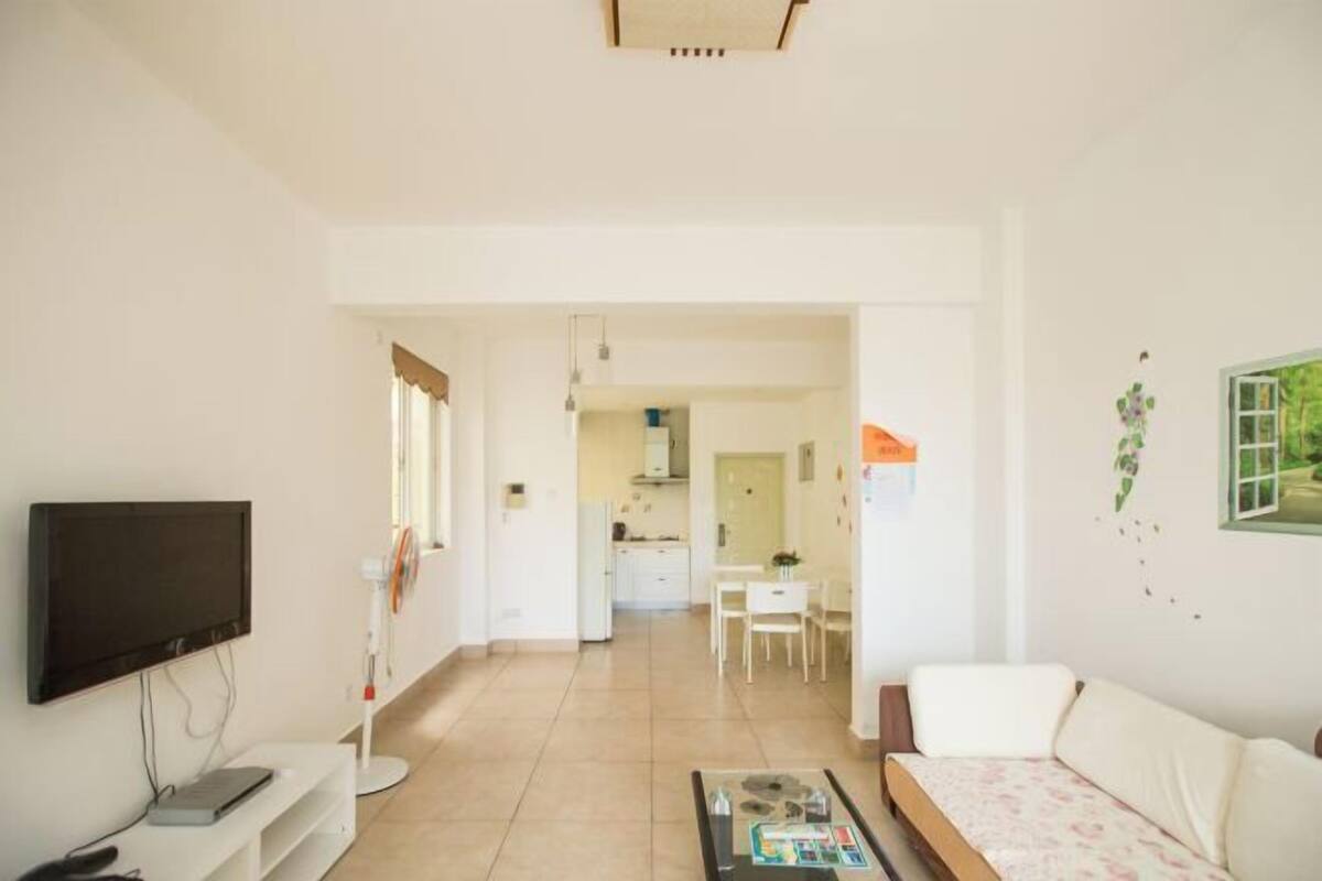 A living room with a TV, a sofa, a coffee table, and a dining area in the background.