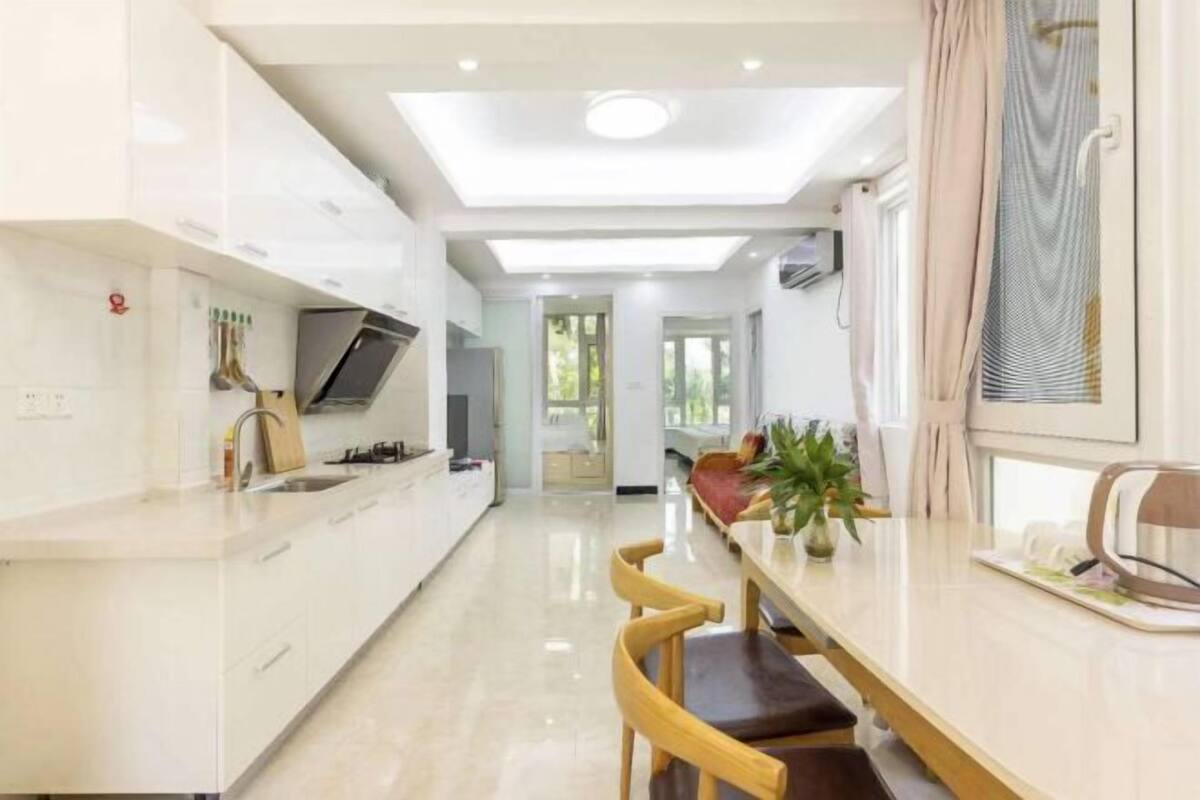 A modern kitchen with a central island, a dining area with a table and chairs, and a view of the outdoors.