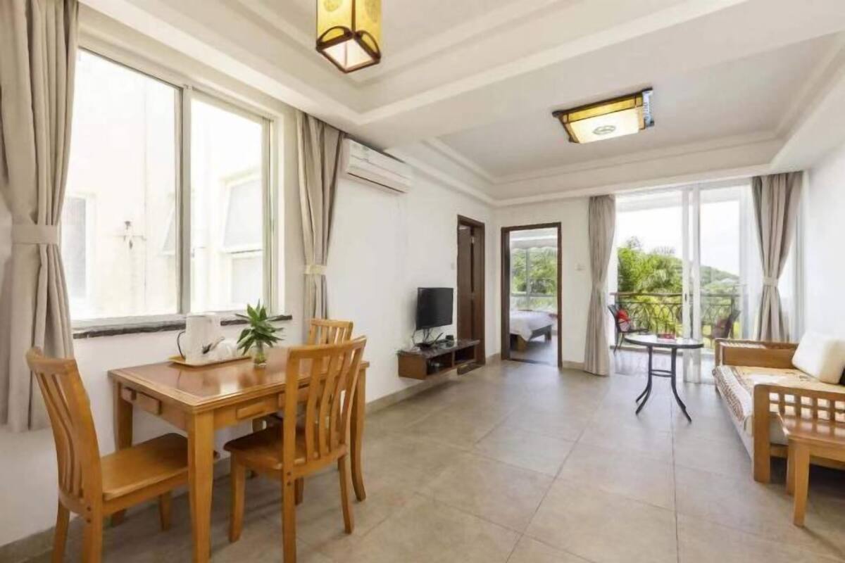 A spacious living area with a dining table, chairs, a sofa, a TV, and a balcony with a view.