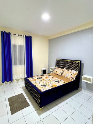 A bedroom with a bed, curtains, a bedside table, and a floor lamp. - Large furnished apartment in Bastos (Yaoundé)