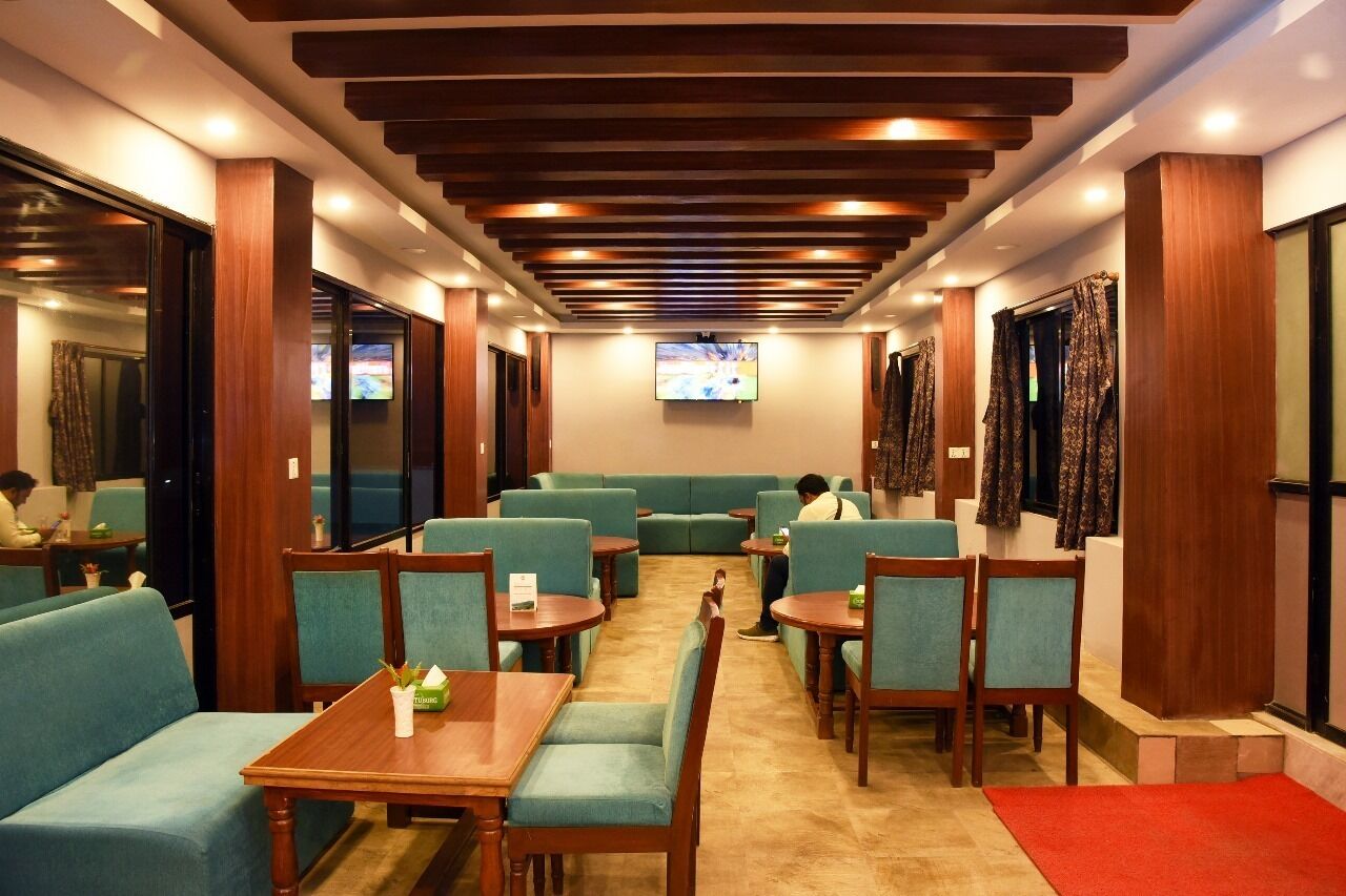 A restaurant with green upholstered seating, wooden tables, and a TV mounted on the wall.