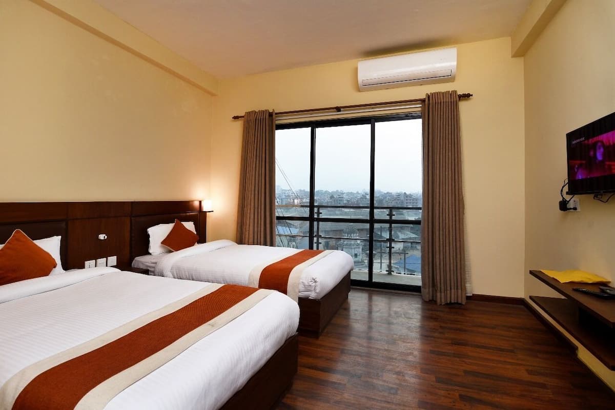 A hotel room with two beds, a large window with curtains, an air conditioning unit, and a television on the wall.