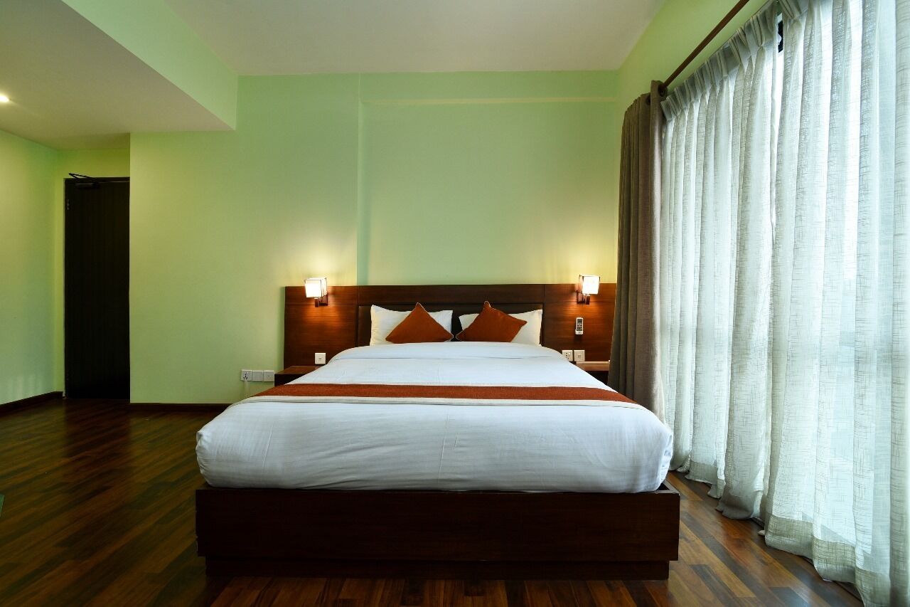 A hotel room with a large bed, wooden headboard, two bedside lamps, and a window with curtains.