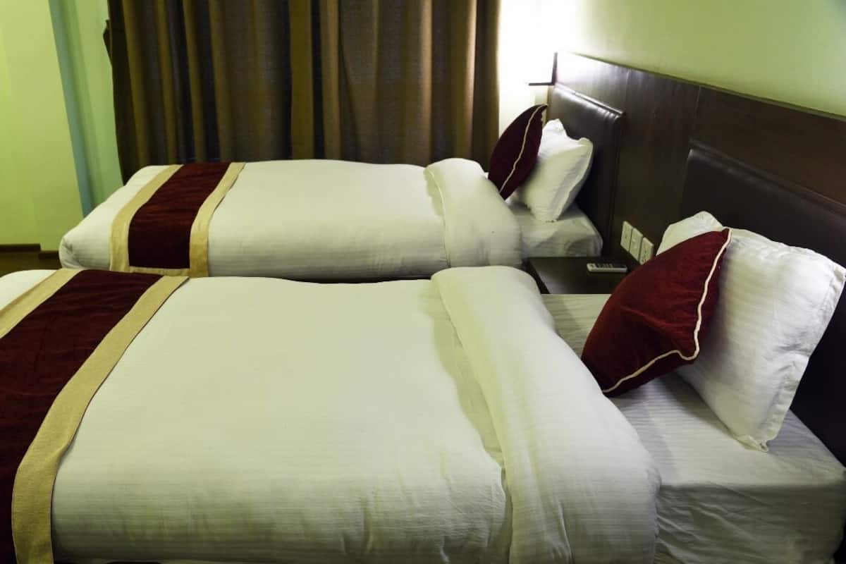 Two single beds with white linens and red accents, a wooden headboard, and a remote control on the nightstand.
