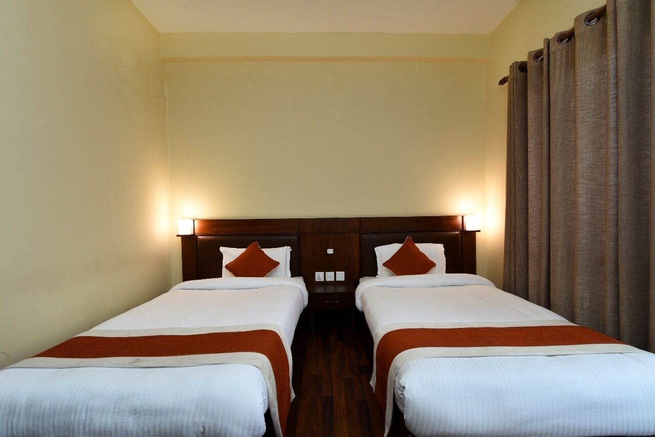 A hotel room with two single beds, wooden headboards, and a large window with curtains.