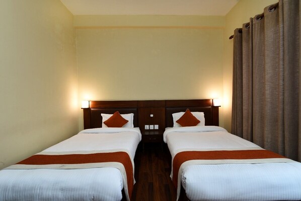 A hotel room with two single beds, wooden headboards, and a large window with curtains.