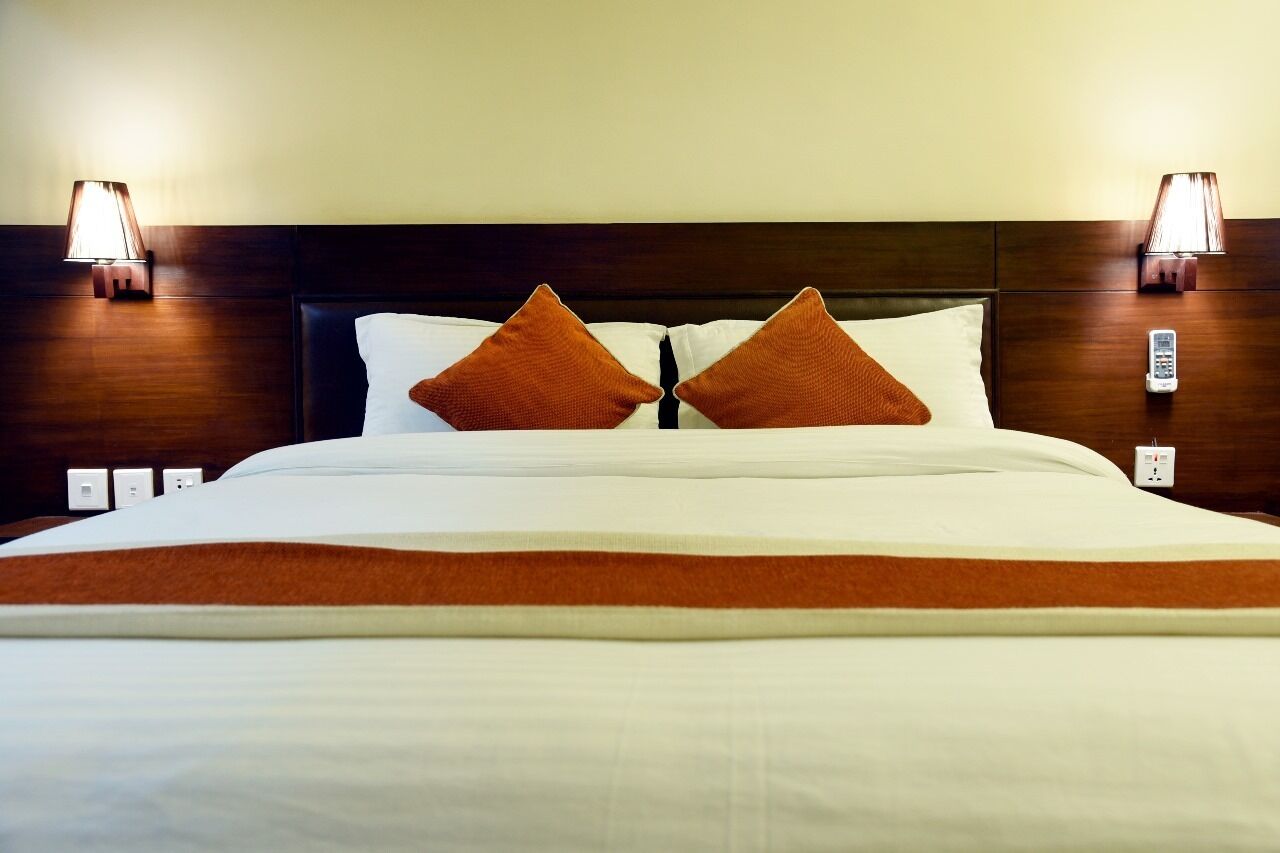 A neatly made bed with white linens and two brown pillows, flanked by two wall-mounted lamps.