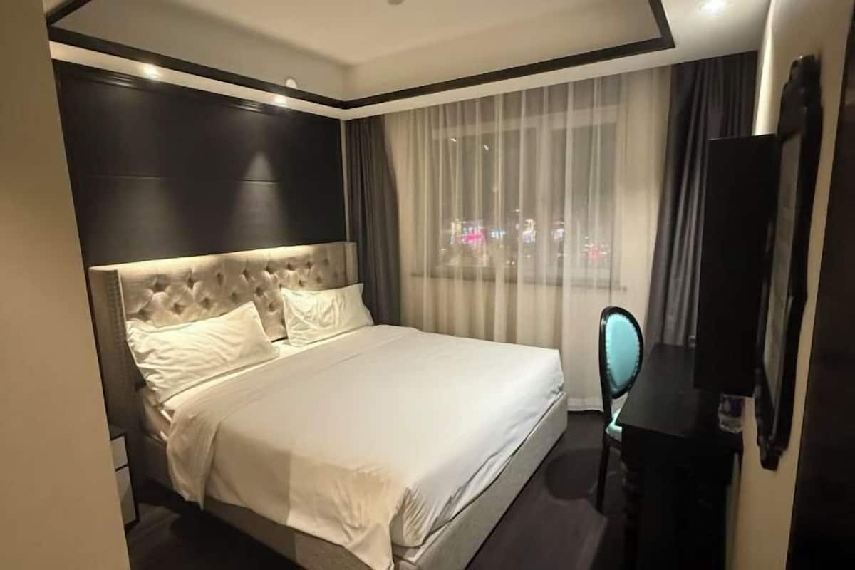 Hotellihuone, jossa on suuri sänky, taulutelevisio, peili ja näkymä kaupunkiin yöllä.