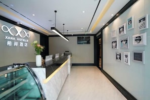 A hotel reception area with a modern design, including a reception desk, a wall-mounted sign, and a series of framed pictures on the wall. - Xana Hotelle (Beijing Changping Metro Station, China University of Petroleum‑Beijing) (Beijing)