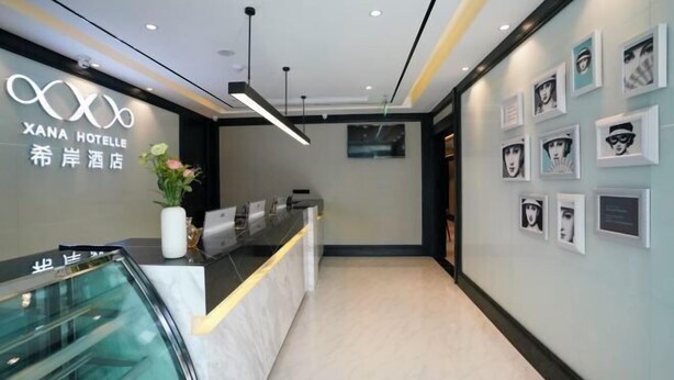 Un'area reception di un hotel dal design moderno, con una scrivania della reception, un ascensore in vetro e opere d'arte incorniciate alle pareti.
