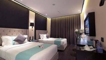 A hotel room with two beds, a flat-screen TV, a desk with a chair, and a vase with flowers.